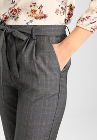 Pantalons à carreaux gris avec une coupe décontractée, dotés d'une taille à nouer et de poches latérales, fabriqués dans un tissu léger au toucher lisse.