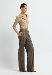 Beige langekleurig shirt met knopen, gecombineerd met wijde bruine geplooide broek en bruine puntige hakken. Eenvoudig ontwerp en op maat gemaakt fit.