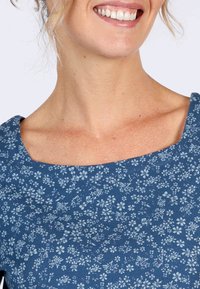 Bluse mit Blumenmuster aus tiefblauem Stoff, mit weitem Ausschnitt und kurzen Ärmeln. Das Muster enthält kleine hellblaue Blumen und Akzente.