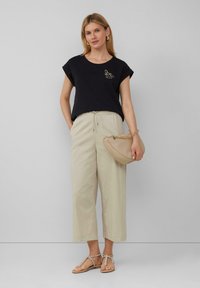 Zwarte katoenen T-shirt met opgerolde mouwen en geborduurd bijgedetailleerd bij, gecombineerd met beige cropped broeken. Bruine sandalen en een beige clutch.