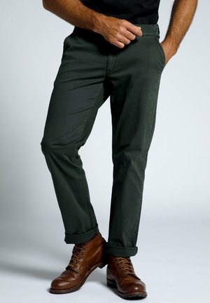 Chinos in cotone verde scuro con un design aderente. Presentano tasche laterali, una texture liscia e orli arrotolati abbinati a stivali marroni con lacci.