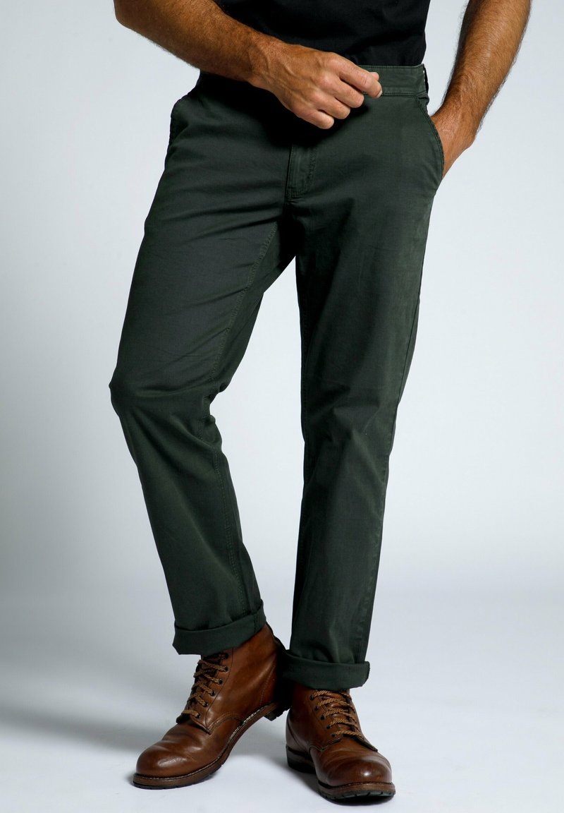 Chinos de algodón verde oscuro con un diseño ajustado. Presentan bolsillos laterales, una textura suave y puños enrollados, combinados con botas marrones de cordones.