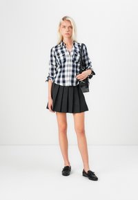 Svart-hvitt rutete skjorte med oppbrettede ermer, kombinert med en plisserte svart skjørt og svarte loafers. Enkle svart veske som tilbehør.