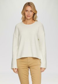 Maglione lavorato a maglia di colore bianco sporco, con scollo rotondo e spalle basse. Abbinato a pantaloni beige slim. Vestibilità casual e rilassata.