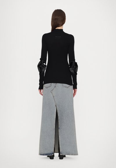 Svart stickad topp med texturerade ärmar och hög hals, tillsammans med en lång ljus tvättad denimkjol med en bakslits och synlig sömnad.