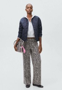 Vadderad navy bomberjacka över en vit crop top, i kombination med vida grå byxor med djurmönster. Grå handväska med en rosa randig accent.