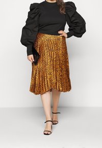 Top nero a coste con maniche a sbuffo, abbinato a una gonna a pieghe con stampa leopardata arancione. Una clutch nera e sandali neri con cinturini completano il look.