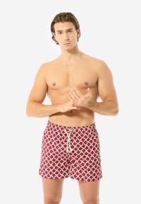 Costumi da bagno rossi con un motivo circolare in bianco e teal, con vita regolabile tramite cordino e una texture del tessuto liscia.