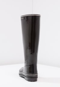 Botte haute en caoutchouc noir avec finition brillante, accent argenté en haut et semelle noire texturée. Idéale pour les conditions humides.
