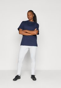 Marinblå bomullströja med en blå logotyp, matchad med vita tights som har en liten logotyp. Svarta träningsskor fulländar outfiten.