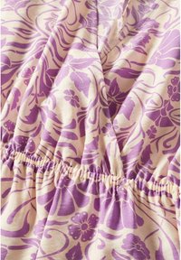 Motif floral violet sur un tissu crème clair avec un détail de taille élastique. Texture douce et design fluide avec diverses formes de feuilles et de fleurs.