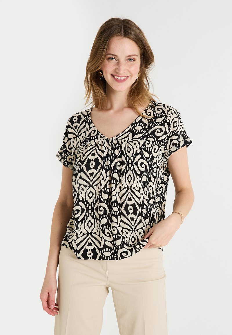 Blusa de manga corta con un estampado en espiral negro y crema, diseño de escote en V y tela ligera, combinada con pantalones beige.