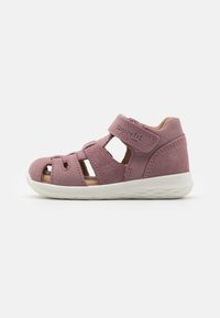 Pink suede sandal featuring a closed toe, multiple cutouts, adjustable Velcro strap, and a white rubber sole for grip and comfort.