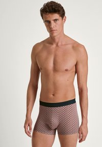 Boxershorts mit einem geometrischen Muster in Rot und Weiß, ausgestattet mit einem schwarzen elastischen Bund. Hergestellt aus weichem, dehnbarem Stoff.