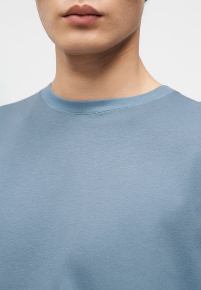 Sweat-shirt bleu clair à col ras du cou avec une texture lisse, présentant un design simple et un col côtelé. Aucun logo ni motif visible.