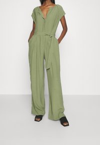 Mono verde oliva con escote en V, mangas cortas, cintura ceñida y piernas anchas. Fabricado con una tela suave y ligera.