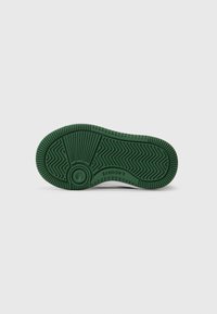 Semelle de chaussure en caoutchouc vert avec des motifs de texture antidérapants et le mot "LACOSTE" en relief le long de la zone de la voûte.