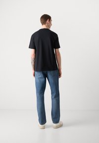 Sort kortærmet T-shirt med rund hals, parret med lyseblå denimjeans og hvide sneakers. Stof ser glat og afslappet ud.