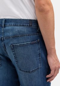 Ciemnoniebieskie jeansy denimowe z lekkim dodatkiem elastanu, z tylną kieszenią ozdobioną metką oraz kontrastowym przeszyciem wzdłuż szwów.