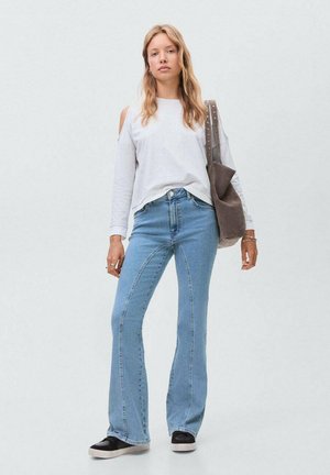 Light gray long-sleeve shirt with cut-out shoulders, paired with high-waisted light blue flared jeans and black slip-on shoes. Brown shoulder bag.