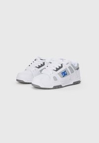 Hvide sneakers med grå accenter, lavet af syntetisk materiale. Har en tekstureret sål, snørebåndslukning og et fremtrædende logo på siden.