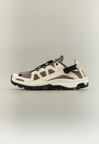 Chaussure de randonnée légère en beige et marron foncé. Présente une tige en mesh, une sangle réglable, et une semelle en caoutchouc avec des crampons profonds pour la traction.