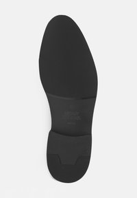 Sole di scarpa nera con superficie testurizzata e righe, timbro del logo e area del tallone sagomata per supporto. Materiale liscio e resistente.