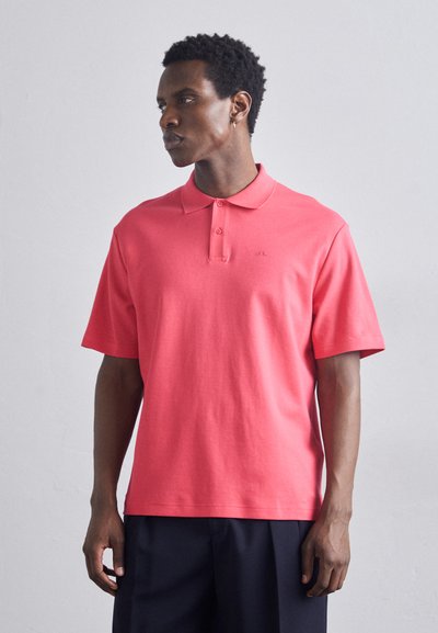 Polo de manga corta en algodón color coral, con un cuello clásico, dos botones y un logo sutil en el pecho. Textura suave y ajuste relajado.