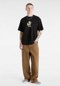 Black short-sleeve t-shirt with a colorful graphic design, paired with light brown wide-leg pants and checkered slip-on shoes.