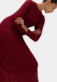 Burgunderfarbenes Langarmkleid aus strukturiertem Spitze, mit einem taillierten Oberteil und einem drapierten Rock, sowie einem runden Ausschnitt.