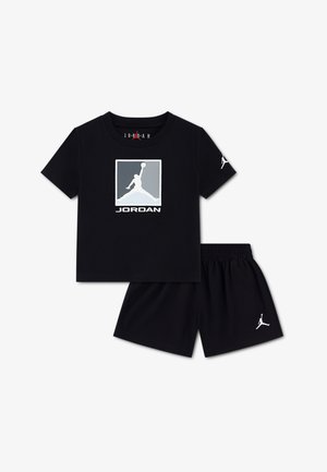 Melna kokvilnas T-krekls ar Jordānijas pelēkas krāsas logotipu, kombinēts ar melniem šortiem, kuros ir balta logotipa akcenta detaļa. Mīksts, elpojošs audums.