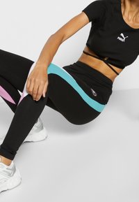 Svarta träningsleggings med ljusblå och rosa sidosträck, tillsammans med en svart kortärmad topp med en logotyp. Slät tygtextur.