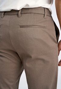 Pantaloni marroni su misura con una texture liscia, caratterizzati da una vestibilità dritta, passanti per cintura e un dettaglio di tasca posteriore sottile.