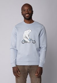 Sweatshirt bleu clair avec un graphique d'un ours blanc montant sur un vélo. Manches et ourlet côtelés avec une texture douce.