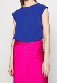 Královsky modrý žebrovaný top s krátkými rukávy, doplněný o jasně růžovou, těsně přiléhající sukni s hladkou texturou a jemným leskem.