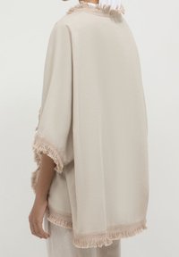 Beige poncho met franjes, gemaakt van lichte stof. Losse pasvorm, met een zachte textuur en zonder zichtbare patronen of hardwaredetails.
