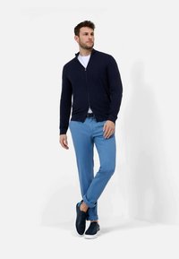 Marinefarbenes Zip-Up-Sweatshirt über einem weißen T-Shirt, kombiniert mit hellblauen Chinos und navyfarbenen Sneakers. Weicher Stoff; lockere Passform; umgeschlagene Bündchen an den Hosen.