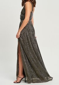 Długa wieczorowa sukienka z metalicznej szarości z bocznym rozcięciem, cienkimi ramiączkami i zwiewnym dołem. Posiada marszczoną górę i fakturę.