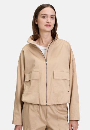 Beige verkürzte Jacke mit einem hohen Kragen, zwei Vorderaschen und einem Reißverschluss. Glattes Material mit lockerer Passform und minimaler Detailgestaltung.