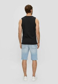 Schwarzes, ärmelloses Oberteil kombiniert mit hellblauen Denims-Shorts. Die Shorts haben einen klassischen Schnitt und sichtbare Gesäßtaschen. Weiße Sneaker runden den Look ab.