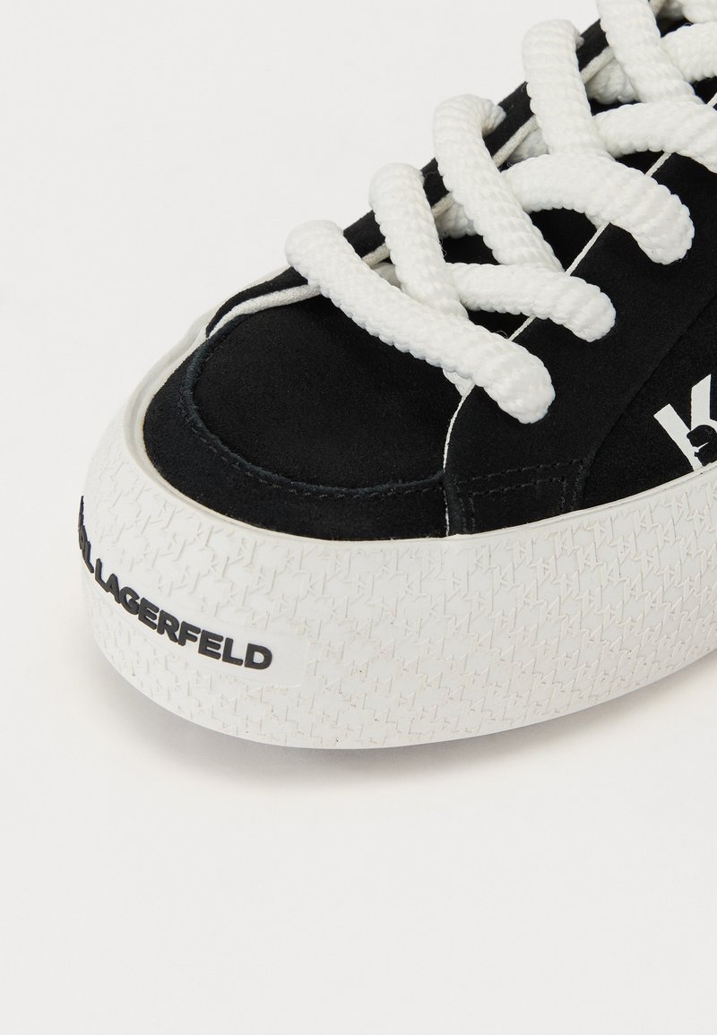 Baskets en suede noir avec des lacets blancs, bout rond, semelle en caoutchouc texturé et logo noir sur le talon. Présente des coutures contrastées.