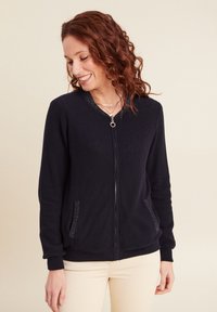 Felpa nera con zip, in tessuto texturizzato, con polsini a coste e due tasche laterali. Presenta un cursore rotondo e un design leggero.