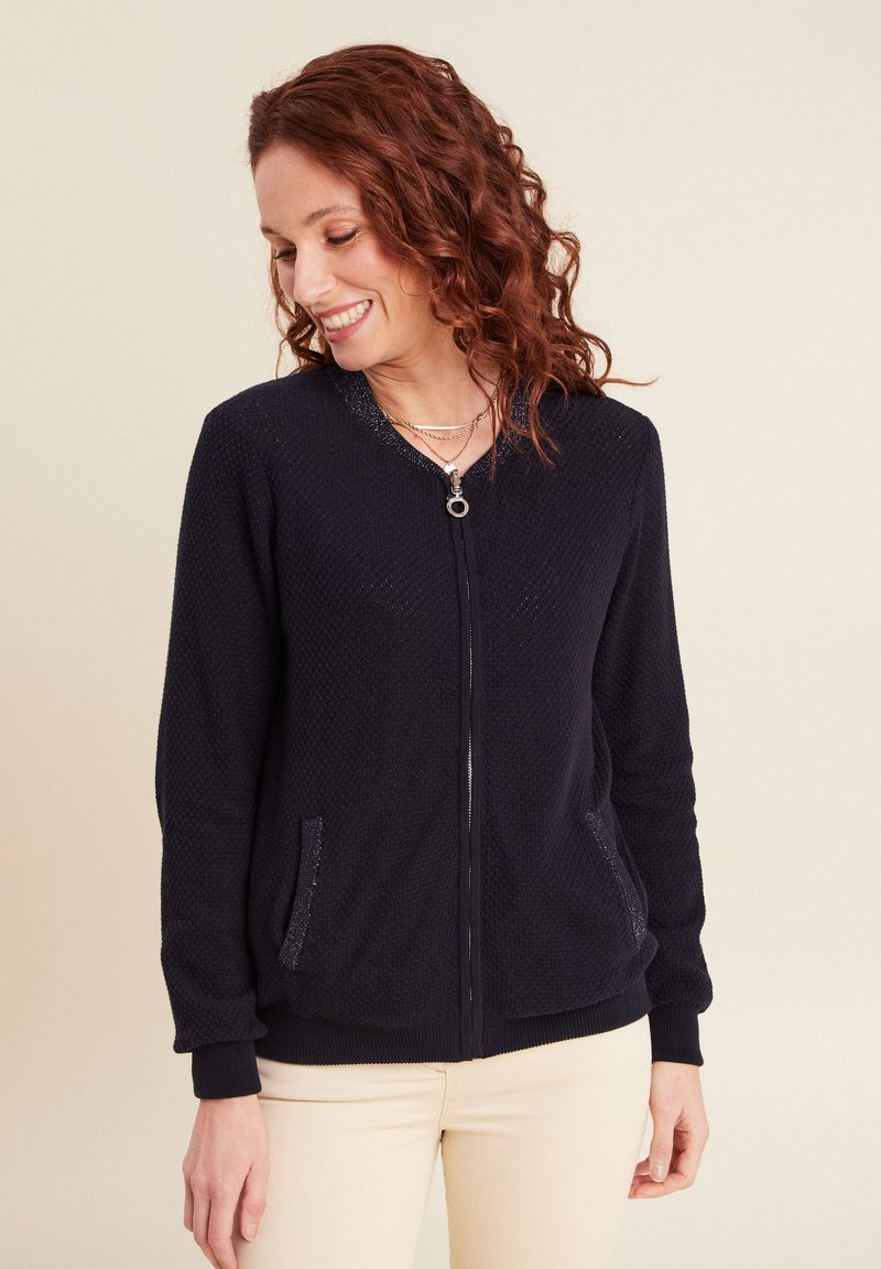 Felpa nera con zip, in tessuto texturizzato, con polsini a coste e due tasche laterali. Presenta un cursore rotondo e un design leggero.