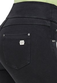 Mustat farkut korkean vyötärön kanssa, takatasku metallisilla yksityiskohdilla ja erottuvilla ompeluviivoilla. Sileä kangaspinta.