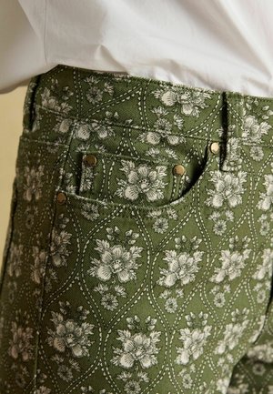 Žalios spalvos raštuotos kelnės su gėlių motyvais, baltomis gėlėmis, tekstūruota medžiaga ir žalvario spalvos sagų akcentais.