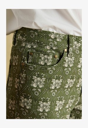 Zielone wzorzyste spodnie z kwiatowym wzorem, białymi kwiatami, teksturowaną tkaniną i mosiężnymi guzikami.