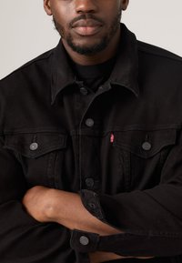 Mustast teksariidest jakk, millel ees nööpidega sulgemine, kaks rinnataskut klappidega ning Levi'si punane silt taskul.