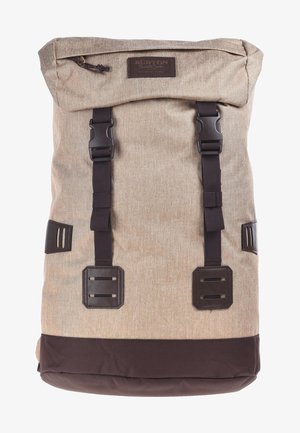 Zaino in tessuto beige con fondo marrone, chiusura arrotolabile, due cinghie nero con fibbie e un'etichetta del marchio. Superficie testurizzata con un design resistente.