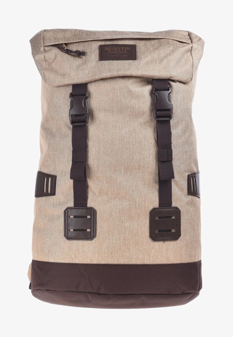 Beżowy plecak z tkaniny z brązowym dnem, zamykany na rolowanie, z dwoma czarnymi klamrami i naszywką marki. Teksturowana powierzchnia o wytrzymałej konstrukcji.