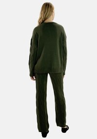 Overdimensioneret olivengrøn strikket sweater med teksturerede ærmer kombineret med matchende ribstrikkede bukser med kabelmønster. Begge dele har en afslappet pasform.